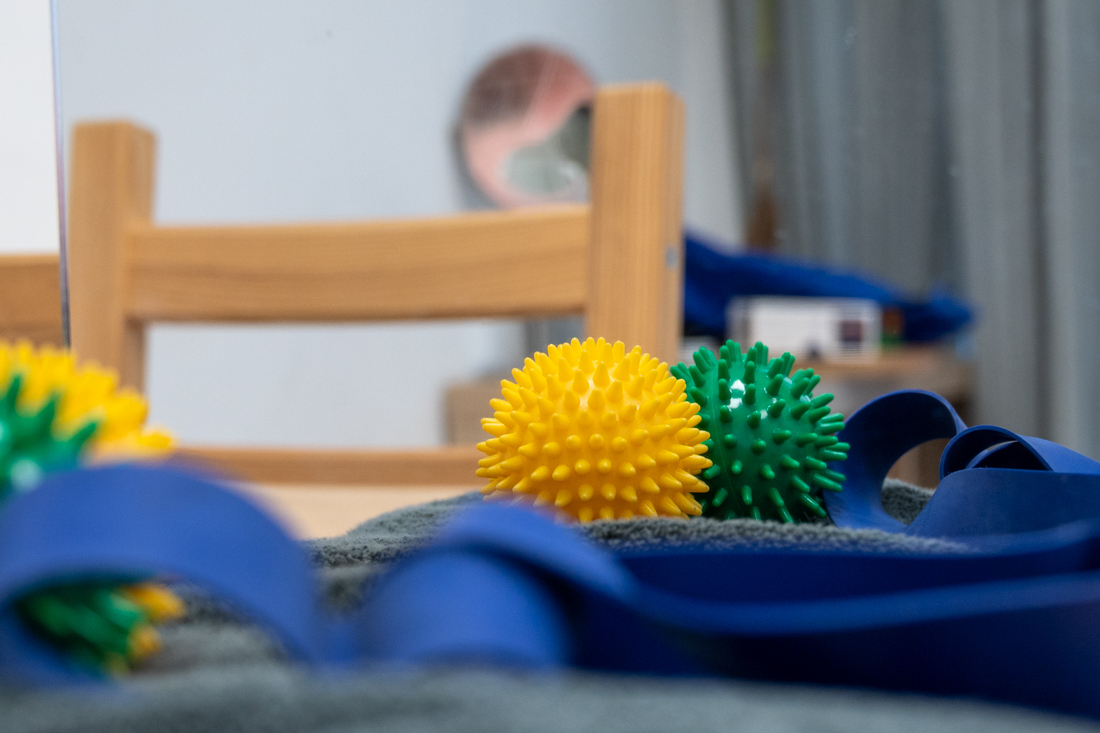 Handtherapie: eine erwachsene Hand drückt in einen Knetball, daneben ein handtrainer